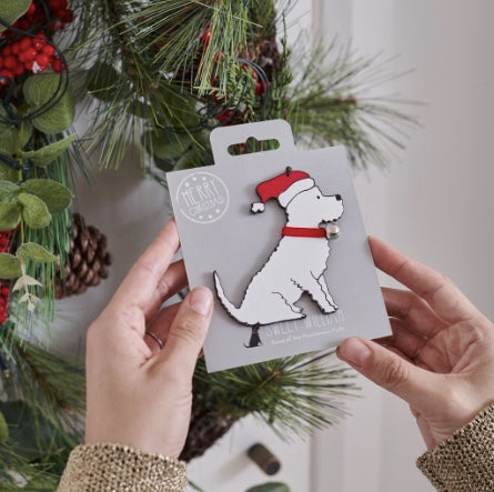 Dog-shaped ornament on a card held by hands with a Christmas wreath in the background